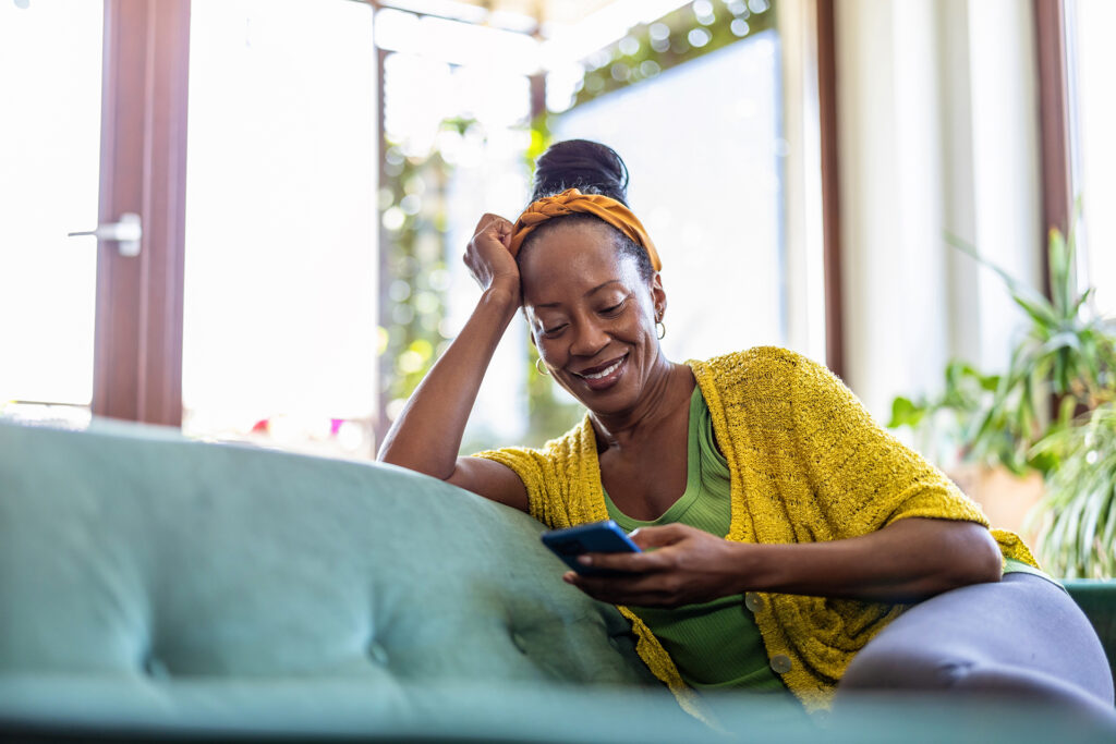 Woman using smartphone while relaxing on sofa at home