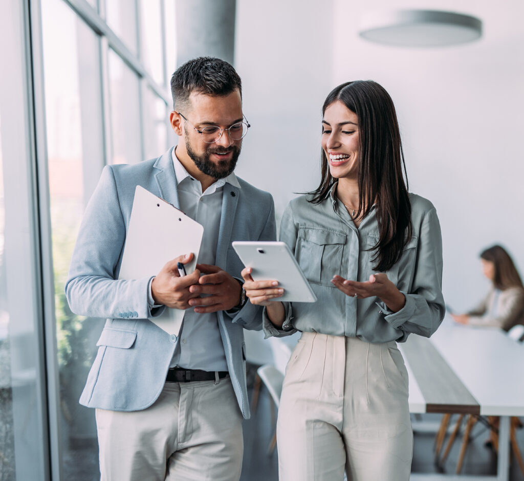Shot of a two confident business persons talking in the work place. Two colleagues using a digital tablet while walking in a modern office. Businessman and businesswoman in meeting discussing business strategy. Business coworkers working together in the offic